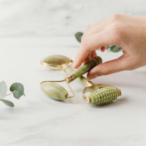 Close-up of a hand holding jade rollers on a marble surface for skincare and wellness.