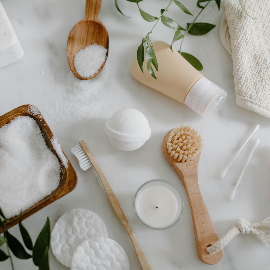 Flat lay of natural spa essentials including salts, soap, brush, and greenery.